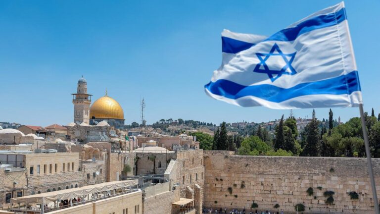 An Israeli flag blows in the wind from an elevated view of the Western Wall. Jewish orthodox believers read the Torah and pray facing the Western Wall, also known as Wailing Wall or Kotel in Old City in Jerusalem, Israel. It is small segment of the structure which originally composed the western retaining wall of the Second Jewish Temple atop the hill known as the Temple Mount to Jews and Christians.